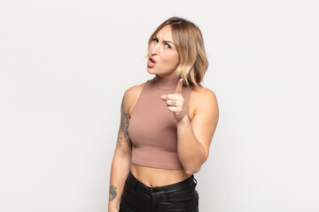 young pretty woman pointing at camera with an angry aggressive expression looking like a furious,...