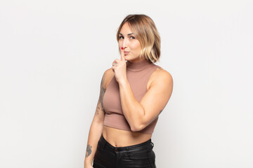 young pretty woman asking for silence and quiet, gesturing with finger in front of mouth, saying...