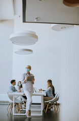Mature businesswoman with protective mask using digital tablet in office
