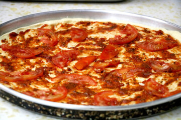 view of preparation of pizza in kitchen with pizza souse and tomato