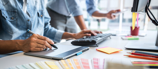 Two colleague creative graphic designer working on color selection and color swatches, drawing on graphics tablet at workplace with work tools and accessories