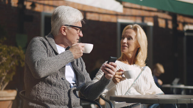Senior couple drinking coffee and using mobile phone in outdoor cafe