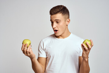 a guy with apples in his hands on a light background in a white t-shirt gesticulate with his hands...