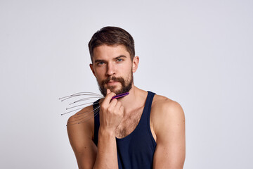 man with a massager for the head and in a blue t-shirt on a light background relaxing beard emotions