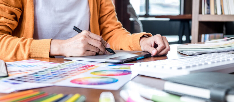 Image of female creative graphic designer working on color selection and drawing on graphics tablet at workplace with work tools and accessories