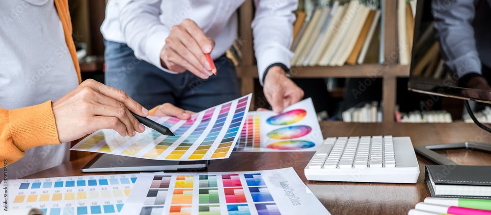 Poster Two colleague creative graphic designer working on color selection and color swatches, drawing on graphics tablet at workplace with work tools and accessories