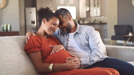 Mid adult couple expecting a baby while husband caresses the belly of his pregnant african woman. Happy father hands on expecting mother's baby bump while embracing her on couch. - Powered by Adobe
