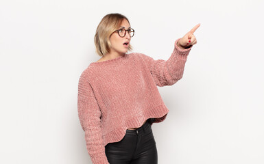 young pretty woman feeling shocked and surprised, pointing and looking upwards in awe with amazed,...
