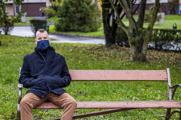 Fototapeta premium A man is sitting on a broken bench in the dripping rain in the local park