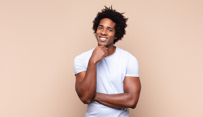 young black afro man looking happy and smiling with hand on chin, wondering or asking a question,...
