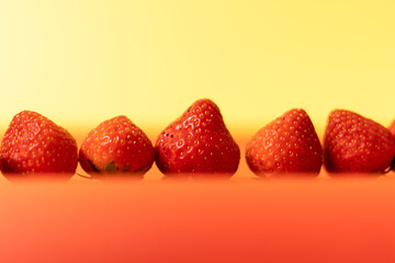 A row of fresh and ripe strawberries on a red and yellow background. Close-up, soft focus.