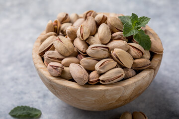Pistachio nuts in a brown bowl on a concrete background. Healthy eating concept