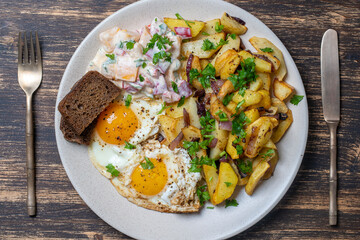 Ukrainian food, fried potatoes with onions, eggs, vegetable salad, black bread on wooden background