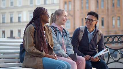 Group of positive international friends sitting on bench and communicating