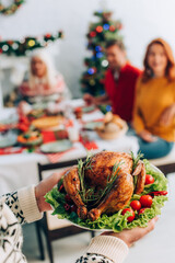 Fototapeta premium senior man holding delicious roasted turkey near family sitting at festive table