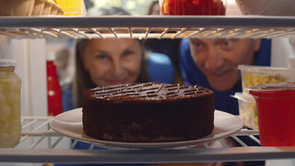 Senior couple taking cake from refrigerator for anniversary party
