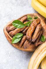 Sun dried bananas in wooden bowl on stone background. Copy space. Superfood, vegan, vegetarian concept.