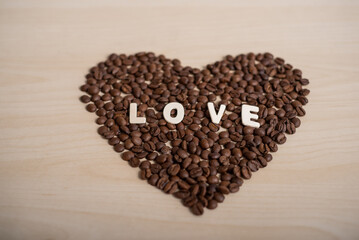 Coffee beans in the shape of a heart and the inscription love on a wooden table