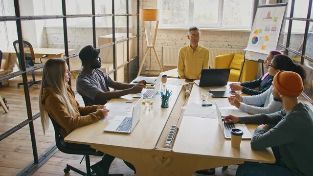 Tracking shot of young coworkers with team leader discussing after pandemic plan, sitting in cozy office