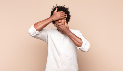 young black afro man covering face with both hands saying no to the camera! refusing pictures or...