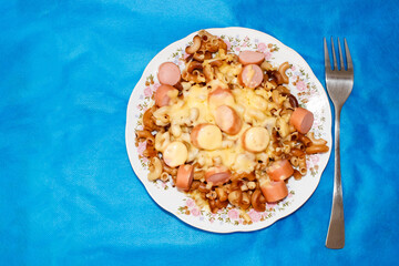 Hot macaroni with sausage and melted cheese on a blue background.