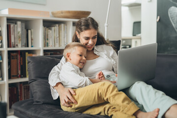 single mother with her child laying on sofa and using computer at home