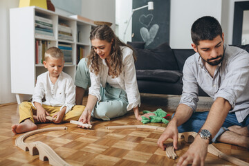 mother and father playing with their child with wooden train toy at home