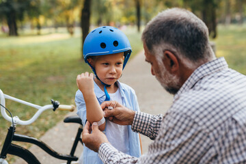 grandfather applying bandage to his grandson arm, boy fallen from the bike