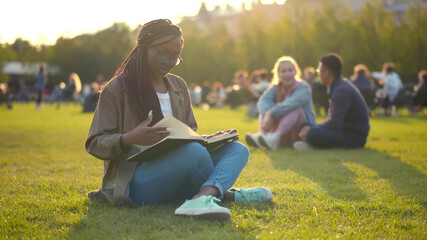 Happy african student lady reading book outdoors in park