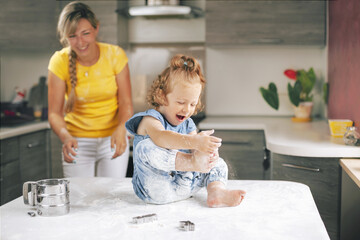 A little girl, soiled in flour, sits on the table and laughs. A girl plays with flour. Blurred background, space for text