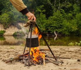 Cooking over a campfire on a trip at the forest river coast.