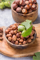 Hazelnuts with peeled hazelnut and leaf  in brown bowl on concrete background.
