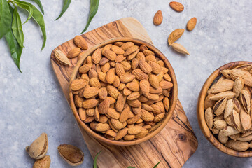 Peeled whole almonds and unshelled almonds in bowl with leaf