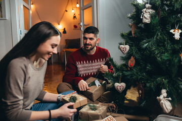 happy young couple decorating christmas presents at home