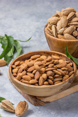 Peeled whole almonds and unshelled almonds in bowl with leaf