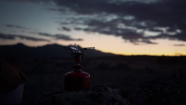 Night time shot of gas camping stove set up in mountain camp. Hiker traveller sparks fire with lighter to warm uo some water for tea or coffee. Adventure lifestyle in great outdoors