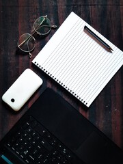 Office desk top down shot. Laptop, notebook, glasses on wooden desk