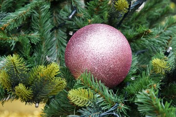 Violet shiny christmas ball on artificial spruce branch. Defocused christmas background. Christimas tree, decoration and lights. Happy New Year and Xmas theme