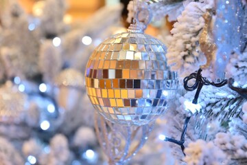 Christmas tree decorated with silvery decorative balls with a burning garland and a blurred gold background.  Decorated Christmas tree with balls and artificial snow. Defocused christmas background.
