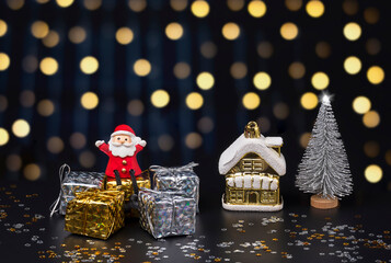Happy Santa Claus doll sitting on gift boxes with Christmas decorations on blurred hanging decorative lights in night background