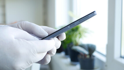Image with Doctor Hands Wearing Protective Gloves Browsing Internet Connection and Sending an Email Using a Smartphone
