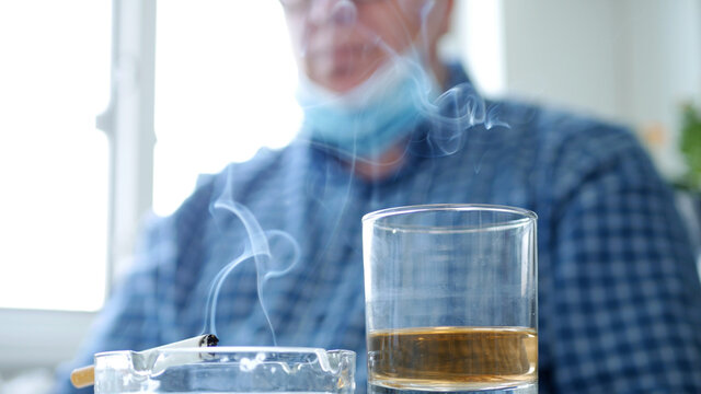 Blurred Image with a Man who Drinks Alcohol and Smokes a Cigarette Wearing Protective Mask on His Facetective Mask on His Face