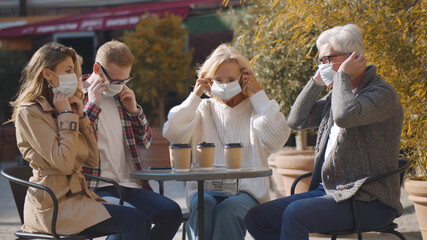 Fototapeta na wymiar Senior couple and adult children leaving street cafe and putting on safety mask