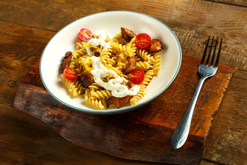 Pasta with chicken and cheese in a gray plate on a table on a wooden stand with a fork.