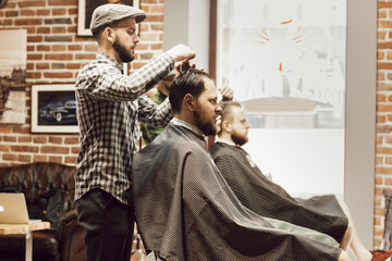 Haircut in the barbershop. Young bearded man getting haircut while sitting in chair at barbershop....