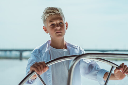 Serious teen handsome blonde boy in white t-shirt and shirt sailing yacht. Education, lessons, studying, skills, growing up concept