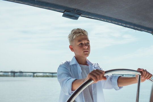 Serious teen handsome blonde boy in white t-shirt and shirt sailing yacht. Education, lessons, studying, skills, growing up concept