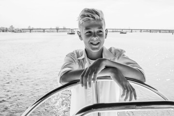 Smiling teen handsome blonde boy in white t-shirt and shirt sailing yacht. Education, lessons, studying, skills, vacation, growing up concept