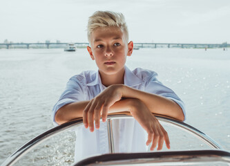 Serious teen handsome blonde boy in white t-shirt and shirt sailing yacht. Education, lessons,...