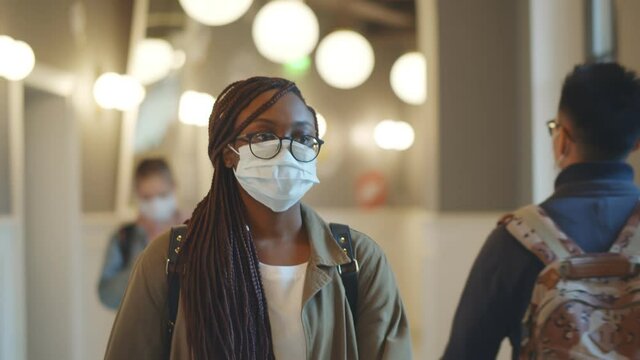 Black Female Student Wearing Medical Mask Walking In University Corridor